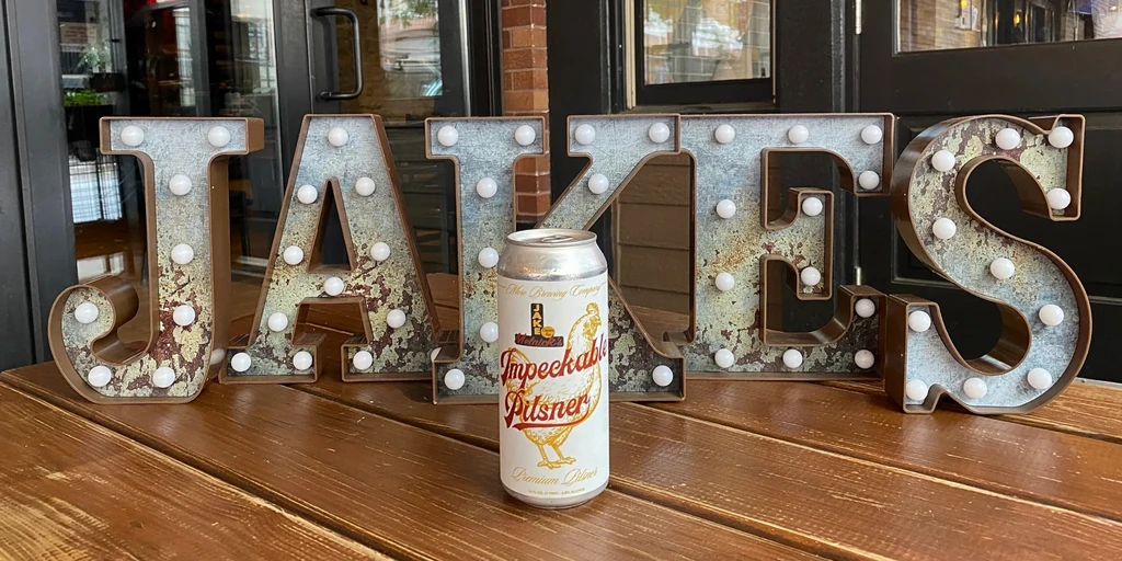 Beer can on a table in front of a "JAKES" sign.