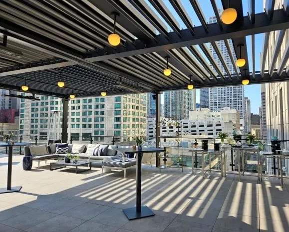 Rooftop bar with dark pergola, light seating, and city view.