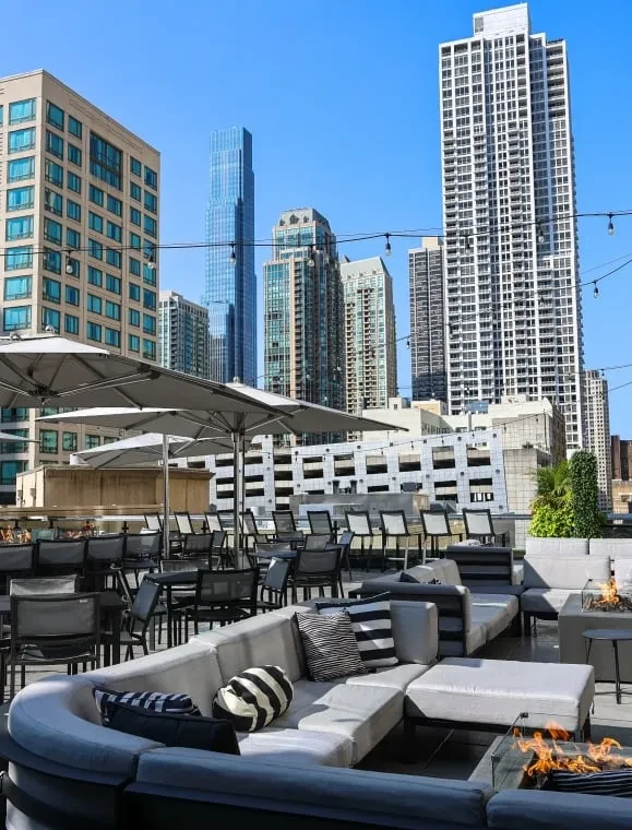 Rooftop bar with lounge seating, fire pit, and city skyline.