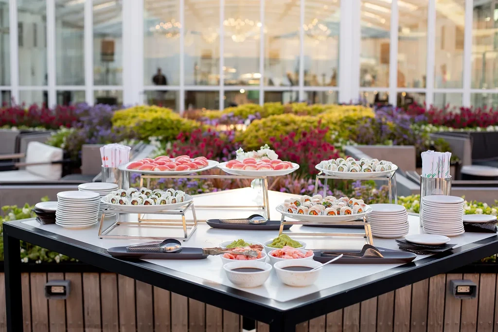 Sushi and sashimi buffet table set outdoors with colorful flowers.