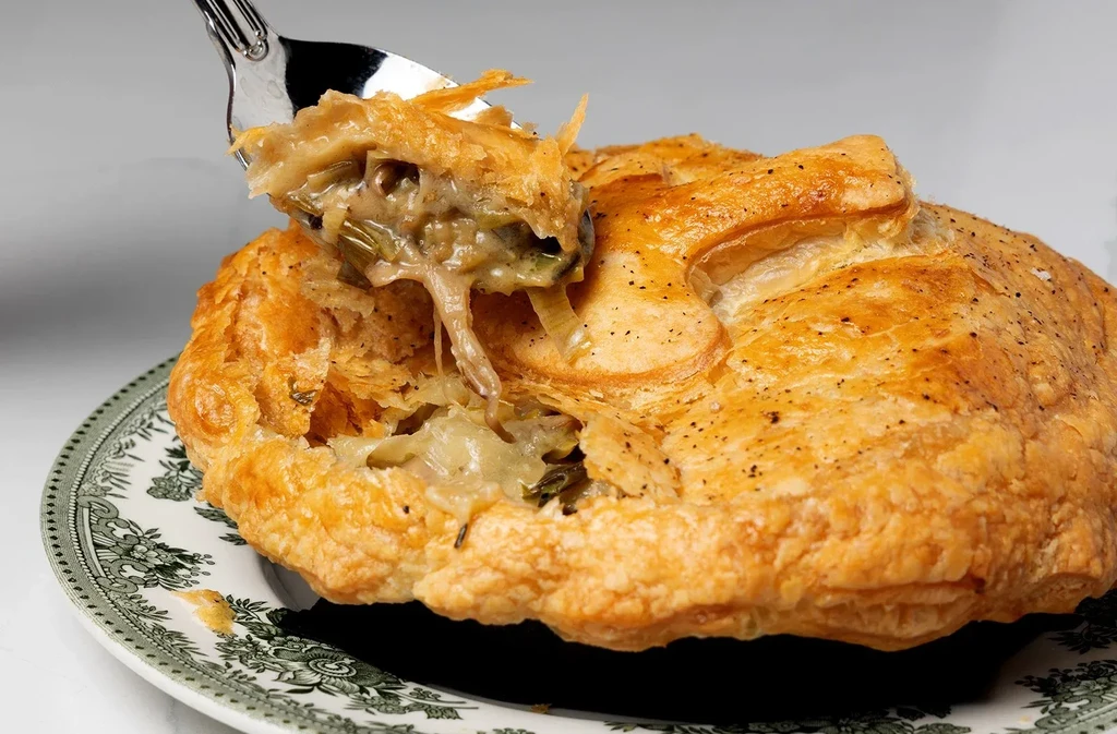Spoon digs into flaky pot pie crust, revealing creamy filling.
