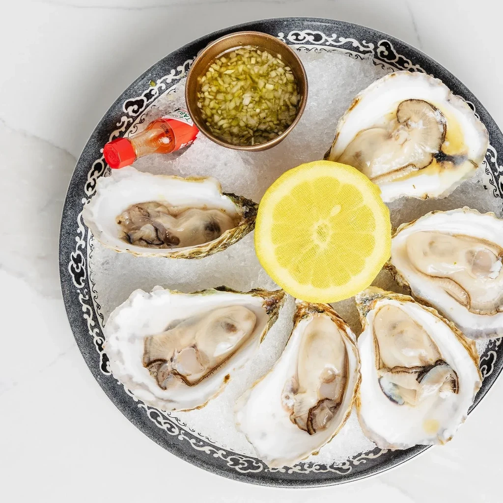 Six fresh oysters on the half shell, lemon, and sauce on ice.