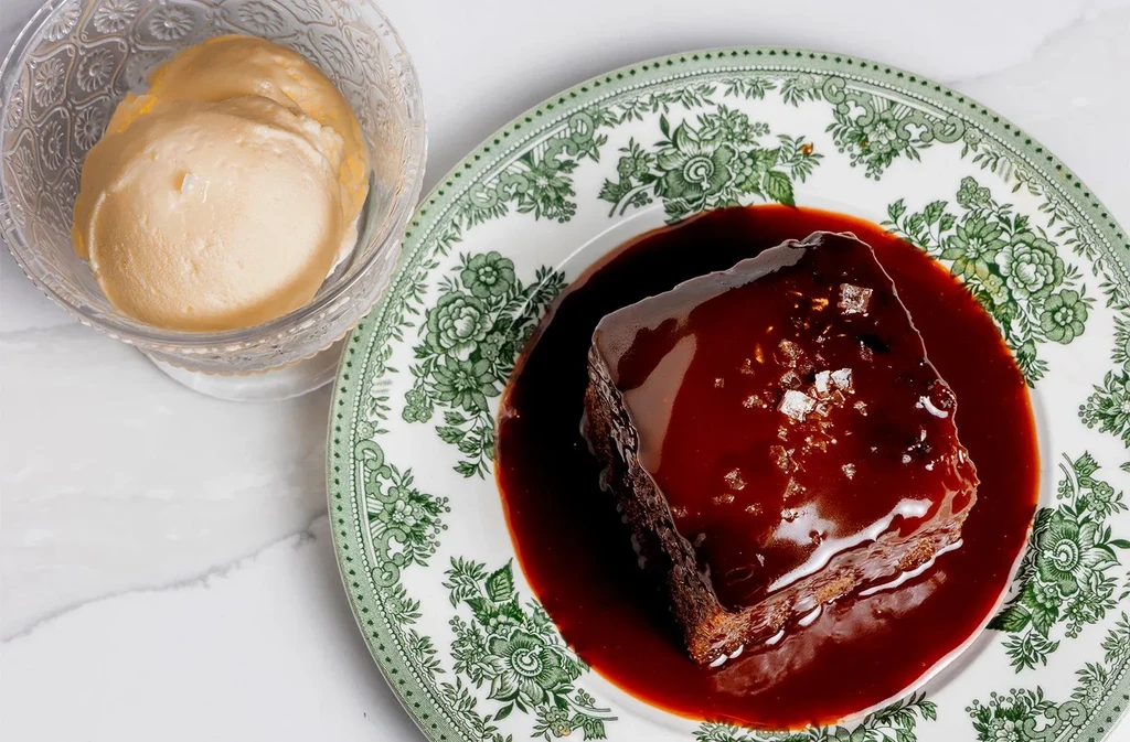 Dark brown cake with sauce, ice cream, on a floral plate.