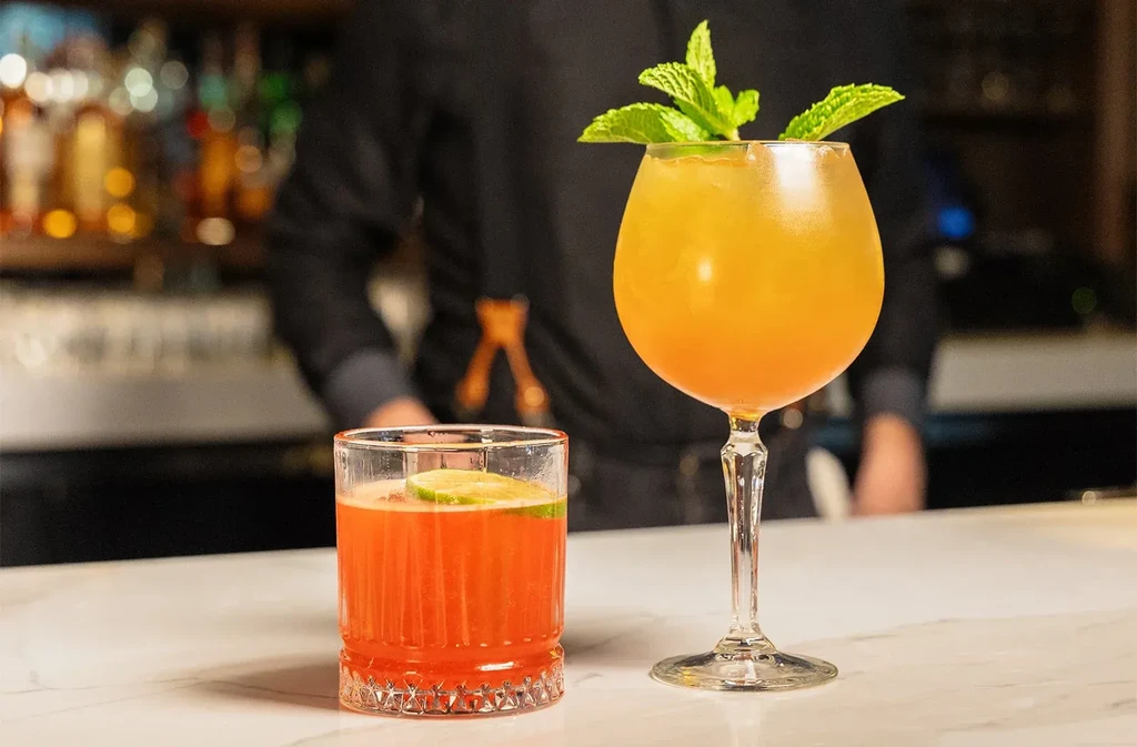 Two vibrant cocktails on a bar counter with a blurred background.