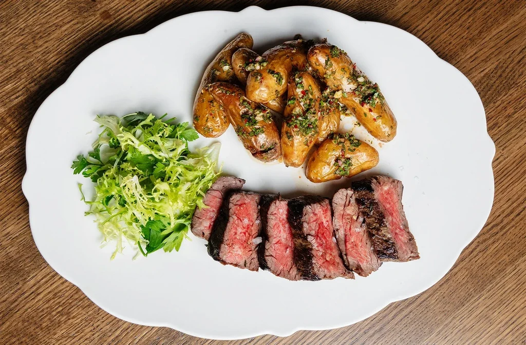 Sliced steak, roasted potatoes with herb sauce, and salad on a plate.