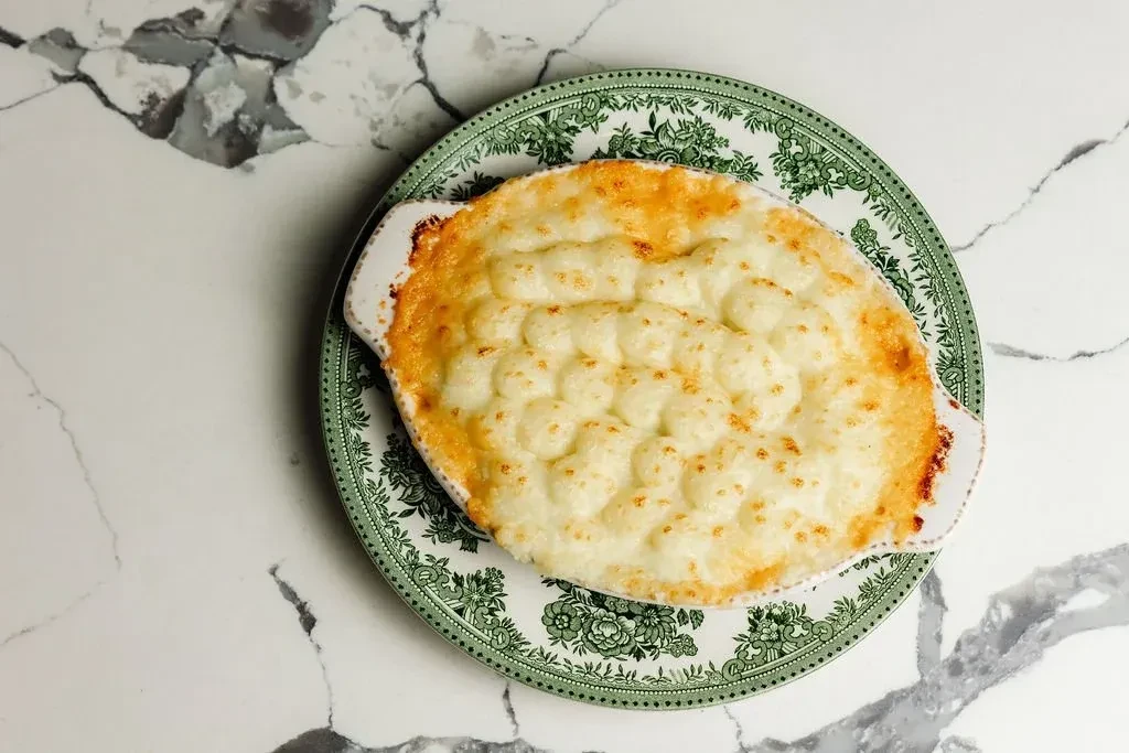 Overhead view of a baked golden-brown gratin in a white oval dish.