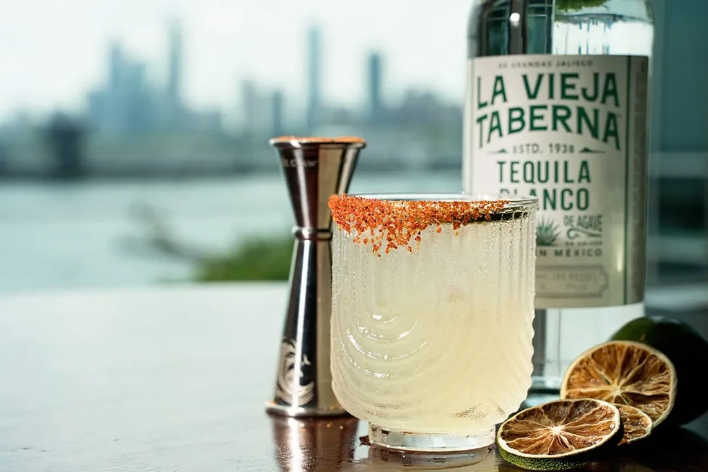 Cocktail with chili salt rim, tequila, dried limes on a wooden surface.
