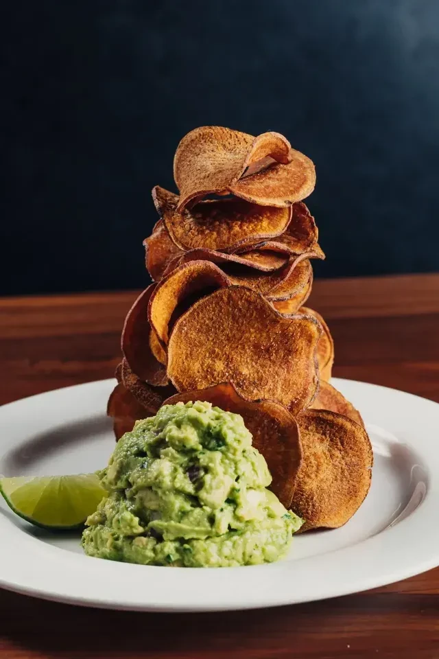 Tall stack of chips, guacamole, and lime wedge on a white plate.