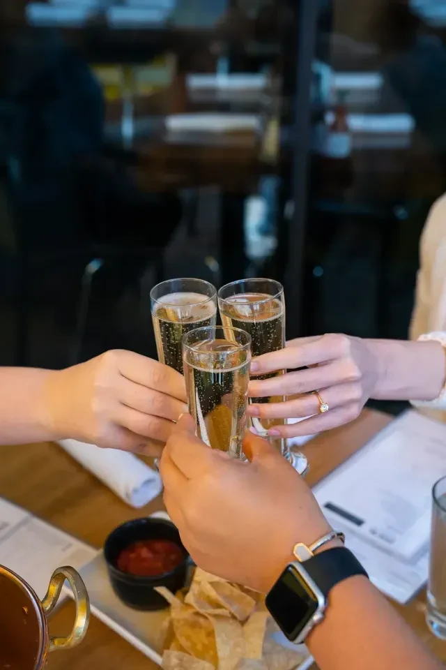 Three hands toast with champagne flutes in a restaurant setting.