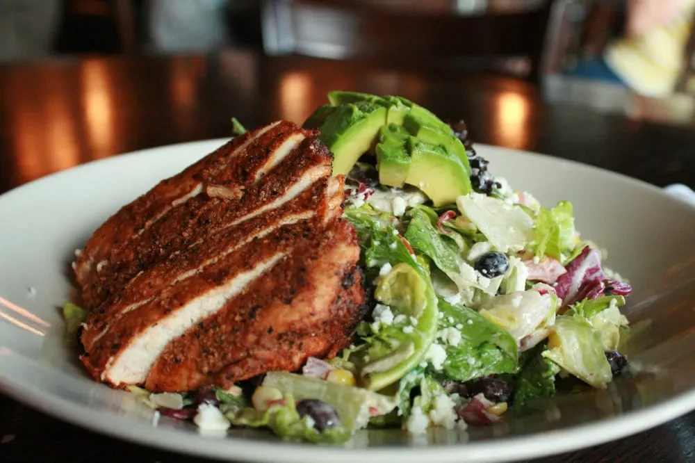 Grilled chicken slices and salad with avocado on a white plate.