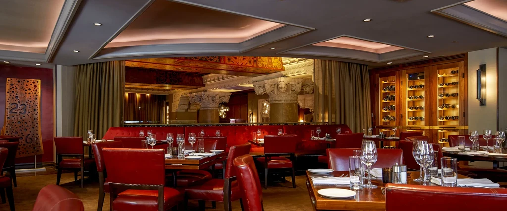 Upscale restaurant interior with red leather seating and wine cellar.