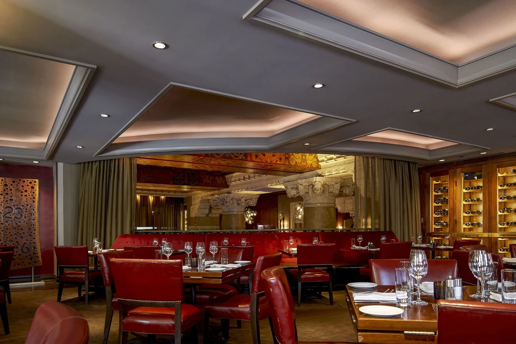 Upscale restaurant interior with red seating, wine racks, and ornate columns.