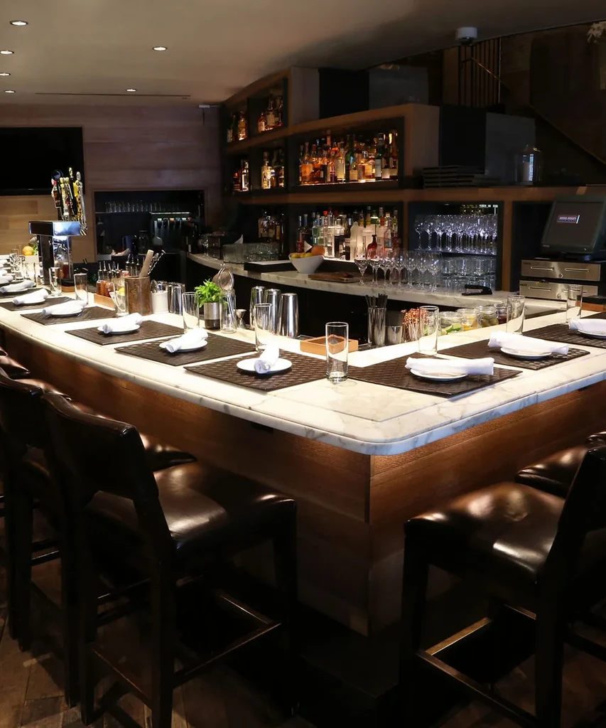 An elegant, empty bar with marble counters and shelves of bottles.