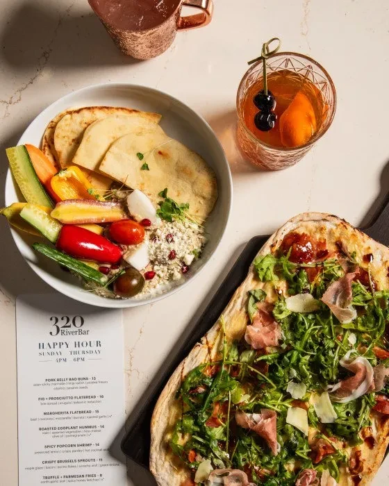 Happy Hour menu, flatbread, salad, and cocktails on a countertop.