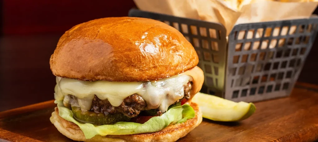 Cheeseburger with melted cheese, lettuce, pickles, fries, and a pickle spear.