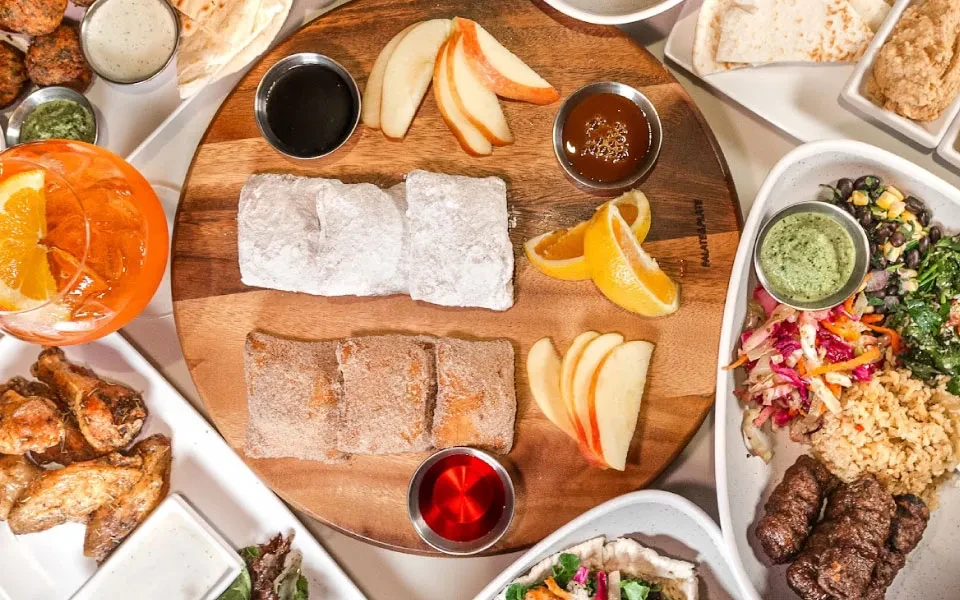 Variety of pastries, fruits, drinks, salad, and kebabs on a table.