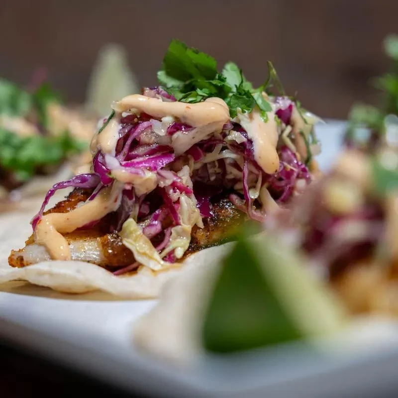 Close-up fish taco with cabbage, sauce, and cilantro on a white tortilla.