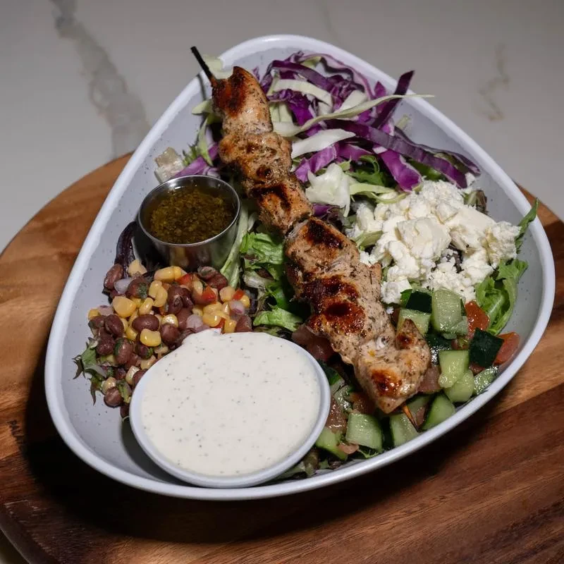 Grilled chicken skewer salad with various vegetables and dressings.