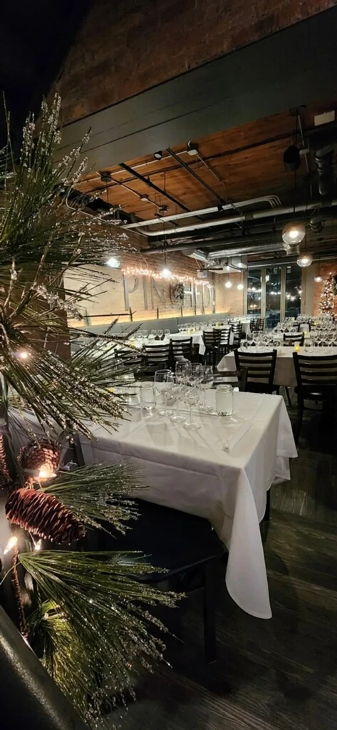 Empty restaurant with white tablecloths, exposed brick, and holiday decor.