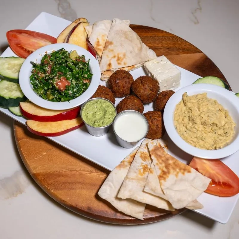 Platter with tabbouleh, falafel, hummus, feta, pita, and vegetables.