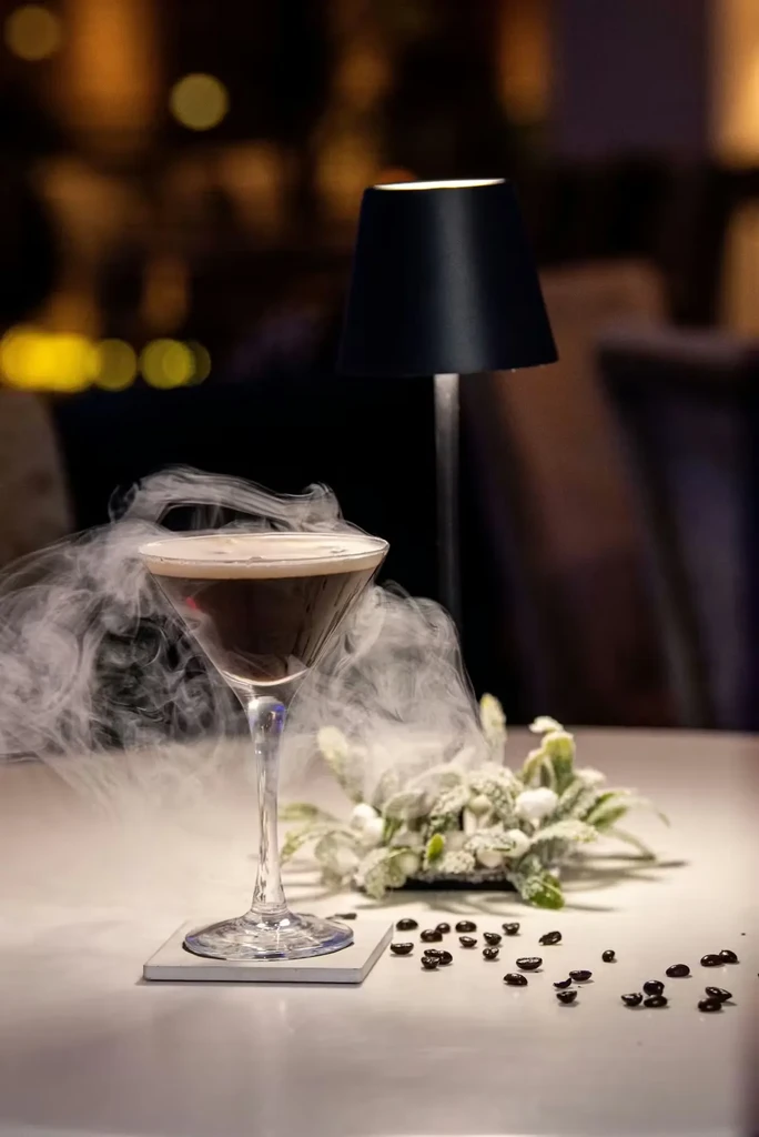 Martini glass cocktail with smoke, leaves, berries, and coffee beans.