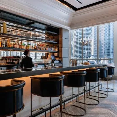 A sophisticated, well-lit bar with a bartender and a cityscape view.