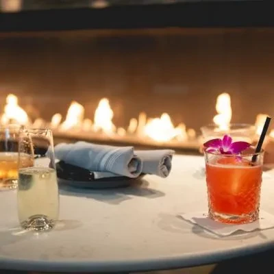 Champagne flute, orange cocktail, napkins on a table by a fireplace.