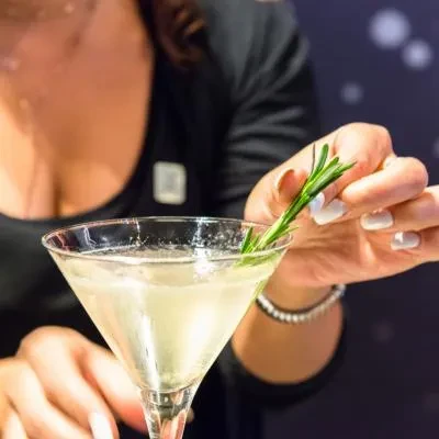 Hands garnishing a clear martini with a sprig of rosemary.