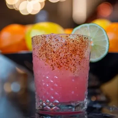Pink cocktail in textured glass with chili-lime salt rim.