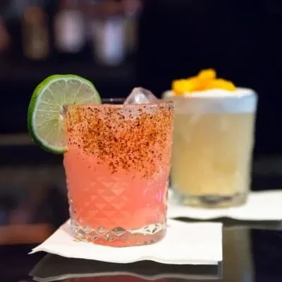 Two cocktails on a dark surface, one pink with lime.