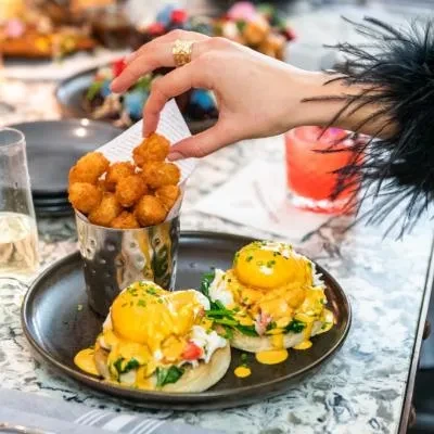Eggs benedict, tater tots, and a hand with a gold ring.