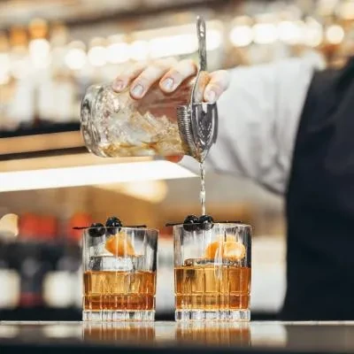 Bartender pours amber liquid from shaker into two garnished glasses.