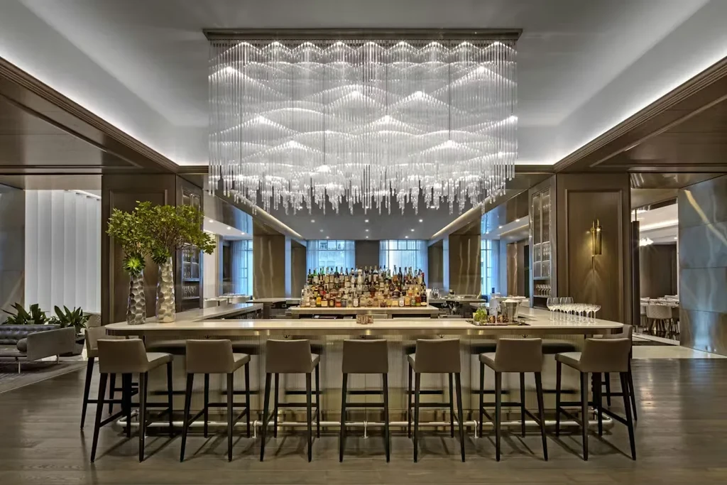 A luxurious, well-lit bar with a curved counter and a large chandelier.