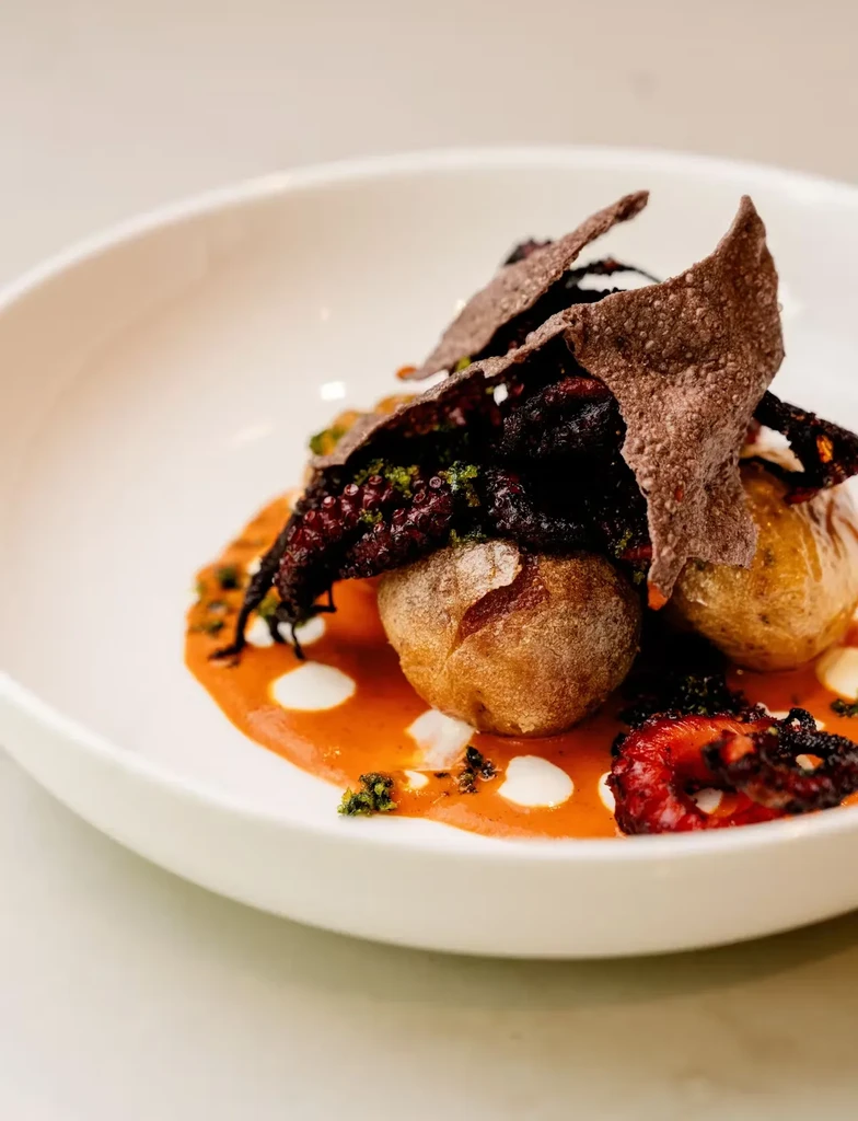 Roasted potatoes, octopus, and crackers on orange sauce with white dollops.