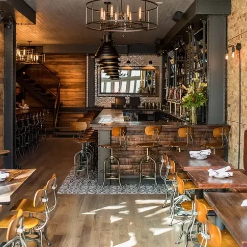 Stylish industrial-chic restaurant interior with bar, tables, and staircase.