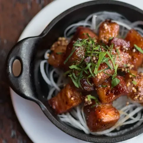 Glazed pork belly with herbs and mustard seeds in a cast-iron skillet.