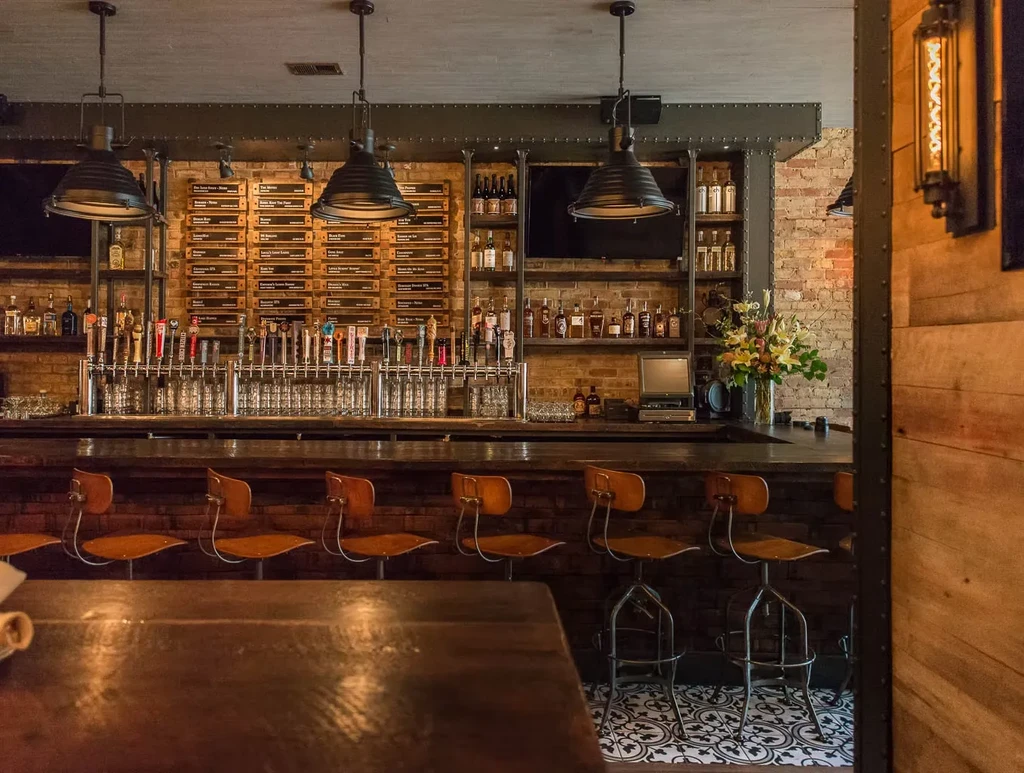 Well-stocked bar counter with beer taps, shelves of bottles, and menu board.