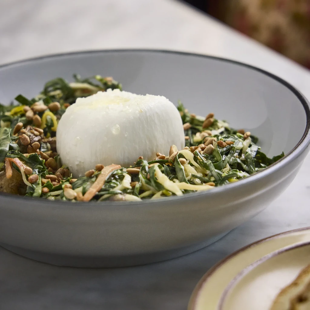 Burrata cheese ball on a bed of greens with sunflower seeds.