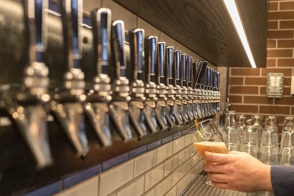 Close-up of beer taps with hand pouring a foamy beer.