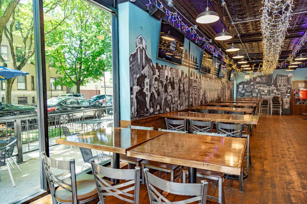 Empty restaurant interior with wooden tables, murals, and industrial lighting.