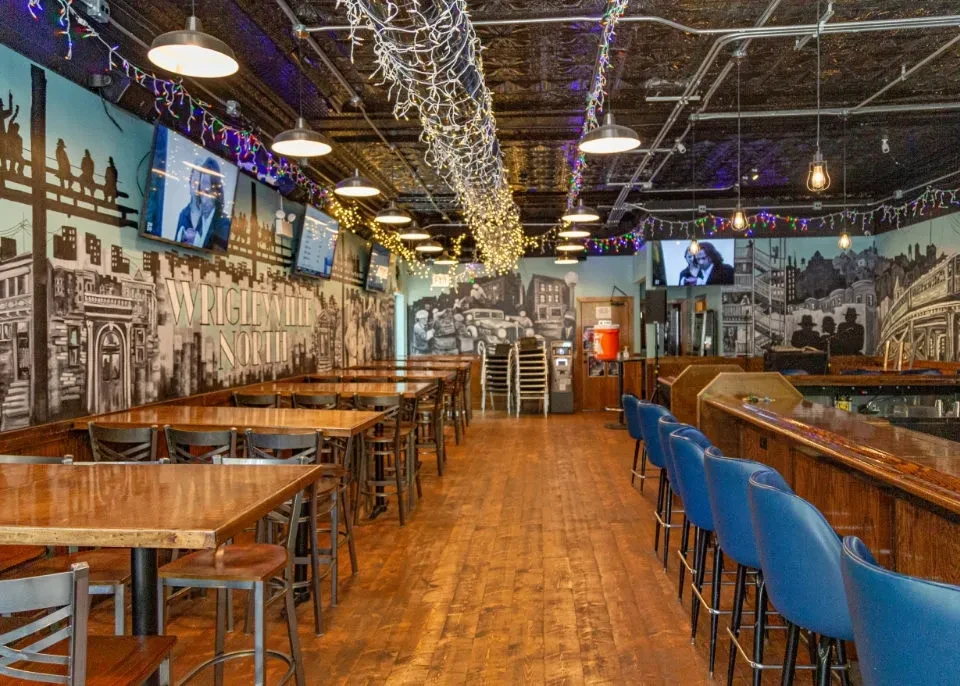 Rustic bar interior with murals, wooden tables, blue barstools.