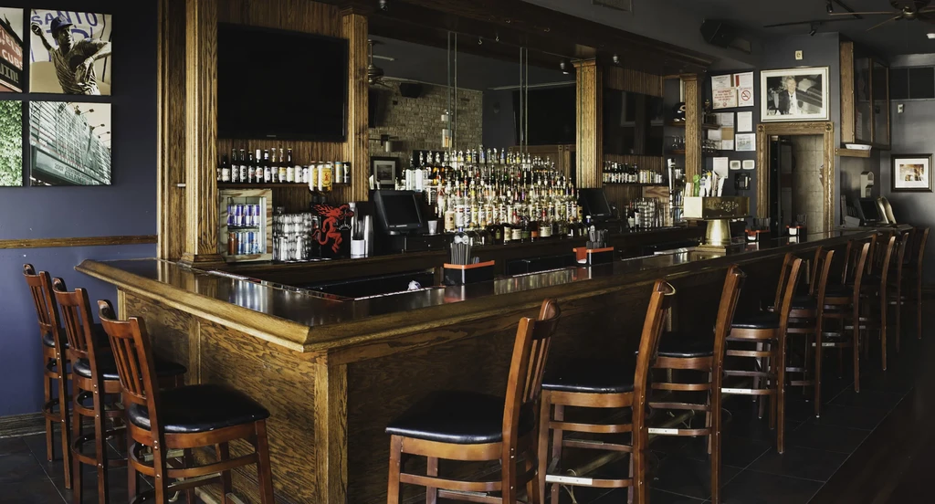 Well-stocked bar interior with mirror, televisions, framed art, and warm lighting.