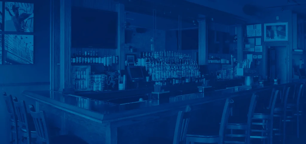 Dimly lit bar interior with stools, liquor bottles, and a TV.