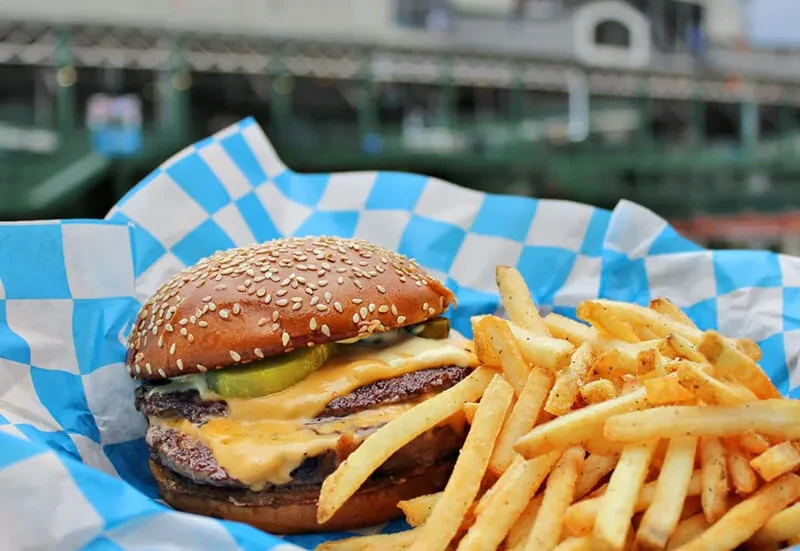 Double cheeseburger and fries in a checkered paper container.