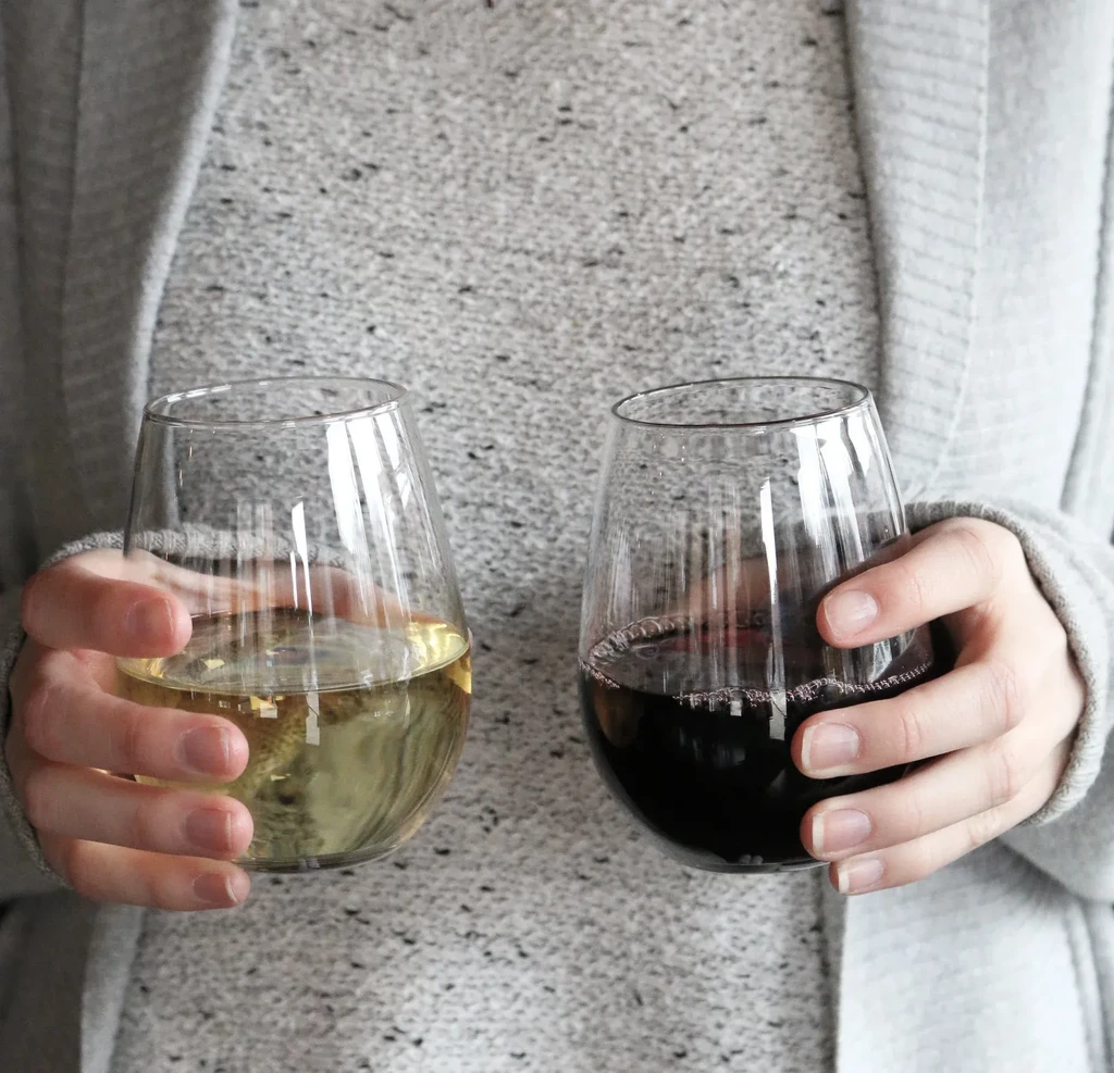 Hands hold two stemless wine glasses, one white, one red.