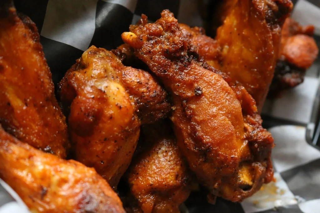 Close-up of crispy, seasoned chicken wings in a checkered paper-lined basket.