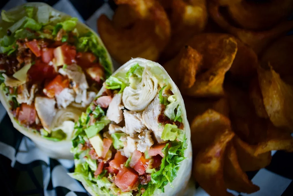Chicken wraps filled with lettuce, tomato, avocado, served with potato wedges.