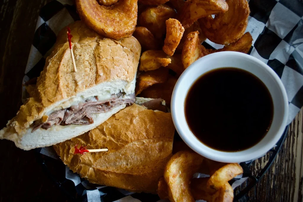 Roast beef sandwich, curly fries, and dipping sauce in a basket.
