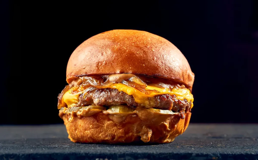 Gourmet burger with beef patty, cheese, caramelized onions, pickles.