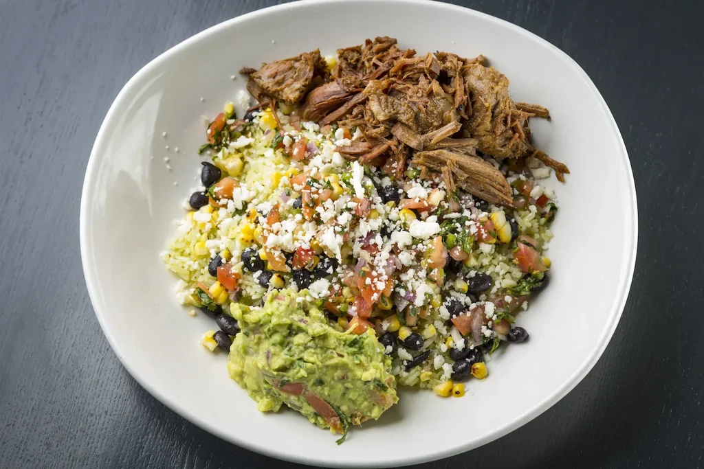 Overhead view of a burrito bowl with meat, rice, beans, and guacamole.